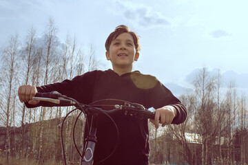 boy holds the handlebars of his bike and smiles in the background light.