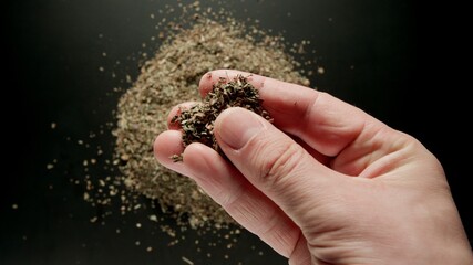 Male hand taking a pinch of dried basil from a pile, top view