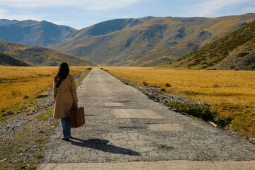 Woman traveler with suitcase is walking on a mountain road.