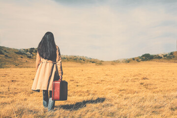 Woman traveler with travel bag walking in a beautiful golden grass field on a sunny day; people, nature and wanderlust concept.