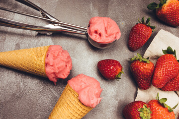 Strawberry ice cream in cookie cone, ice cream scoop, strawberries and berries