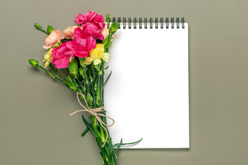 colorful bouquet of different pink carnation flowers, white notebook on green background Top view Flat lay Holiday card 8 March, Happy Valentine's day, Mother's, Memorial, Teacher's day concept 