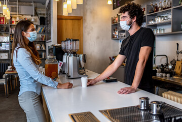 Bar owner working only with take away orders during corona virus outbreak - Young man worker wearing face surgical mask giving takeout coffee to customers - Healthcare and Food drink concept 