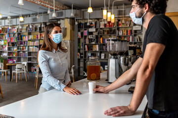 Bar owner working only with take away orders during corona virus outbreak - Young man worker wearing face surgical mask giving takeout coffee to customers - Healthcare and Food drink concept 