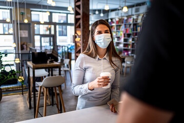 Young woman in cafe public place wearing the protective face mask.Mandatory mask wearing.Safety measures following in the indoor space.Pandemic coffee date.Dating during coronavirus outbreak