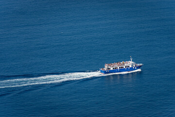 Aerial view of a blue ferry boat with many tourists on board, during sailing to the Cinque Terre in the Mediterranean Sea. Gulf of La Spezia, Liguria, Italy, Europe.