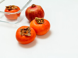 Ripe fresh pomegranate and persimmon fruits with glass bowl.