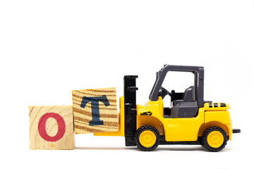 Toy forklift hold letter block T to complete word OT(abbreviation for overtime) on wood background