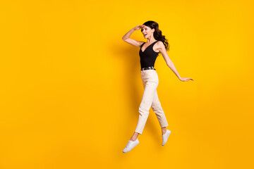 Fototapeta na wymiar Full length body size photo of funny woman jumping keeping hand near forehead looking far isolated vivid yellow color background