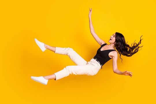 Full length body size photo of woman in stylish outfit falling down shocked amazed isolated on vivid yellow color background