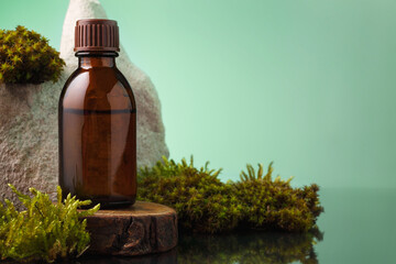 Brown glass bottle of essential oil on wooden stand among the moss against green background, copy space on the right. Essence liquid for skin care or alternative medicine.