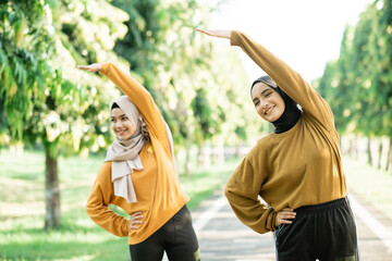 Two asian Muslim girls in headscarves stretch their muscles by raising their hands to exercise...