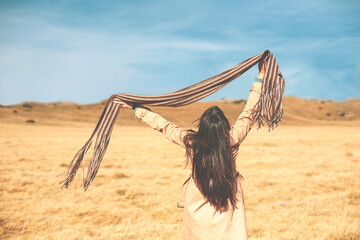 Happy woman is jumping with her scarf up, enjoying life in a golden grass field on a wonderful sunny day.