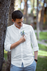 Young handsome groom in a white shirt with a boutonniere in the forest.