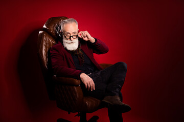 Photo of aged concentrated person hand touch glasses look attentively camera isolated on maroon color background