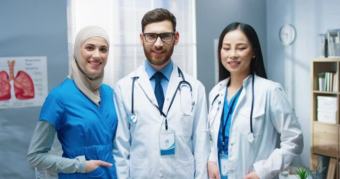 Portrait of multi-ethnic cheerful positive young doctors standing in hospital looking at camera and smiling. Team of healthcare specialists at work in clinic with smile on face. Medical center concept