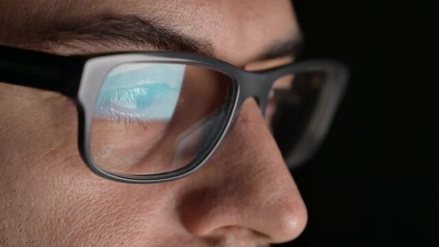 Close up portrait of a software engineer who is working: the eyes are focused on the screen where he is processing the instructions of the program. On the lens of the glasses we see their reflection.