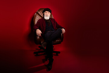 Full size photo of aged person sit in leather chair look interested camera isolated on dark red...