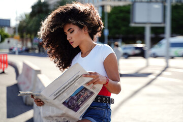 Colombian woman with afro hairstyle reading newspaper on the city street.