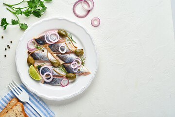Salted herring with spice, herbs and onion on white plate on light stone background with copy space. Marinated sliced fish. Food with healthy unsaturated fats, flat lay