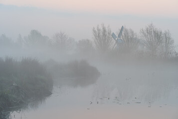 Foggy dawn in the Dutch countryside near a windmill.