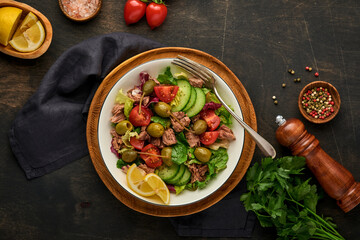 Tuna salad with fresh vegetables, olives, capers and lemon served in bowl on old wooden background. Top view with copy space.