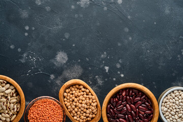 Legumes, red lentils, chickpea, red and white beans assortment in different bowls on dark black...
