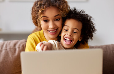 Happy afro american family mother and son watching funny videos on laptop while relaxing in living room at home
