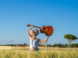 Mujer joven con una guitarra en un campo de trigo 