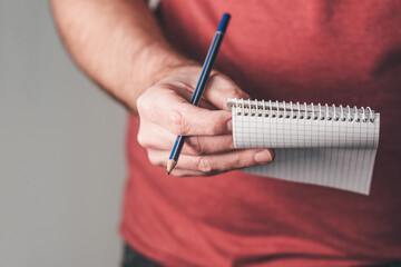 close-up of person holding small spiral notepad and pencil in one hand