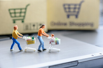 Online shopping / ecommerce concept : Miniature figurine shoppers push a shopping cart on a...