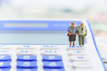 Retirement / pension income tax and social security benefit concept : Older american couple stands near a tax button on a calculator, depicts a single largest expense in retirement e.g pension tax