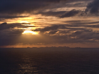 Stunning sunset above Atlantic ocean with dramatic sky of sun breaking through clouds with the silhouettes of Vestmannaeyjar islands on the horizon viewed from Dyrhólaey in southern Iceland.
