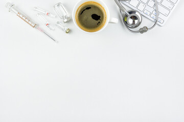 Top or above view, flat lay of physician, professional doctor work table in a hospital, clinical office with a computer keyboard, coffee cup, stethoscope, vaccine ampule vial, syringe with needle