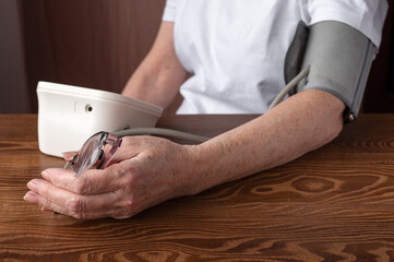 elderly woman suffering from hypertension measures her blood pressure using an electronic monitor. High blood pressure and poor eyesight. Health of the elderly