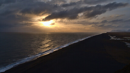 Stunning aerial view over the southern coast of Iceland near Vík í Mýrdal with long black beach Sólheimasandur and Vestmannaeyjar islands on horizon before sunset with sun breaking through clouds.