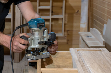 male carpenter works with a hand-held power tool, a milling cutter. Embedding hinges in the...