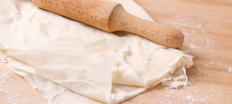 Filo dough and rolling pin on the wooden board. Toned image