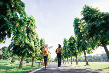 view from below of two girls in veil do outdoor sports while jogging together in the garden with...