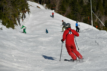 Stowe resort staff in red suit and Group of skiers seen from behind making a turn in Stowe Mountain...