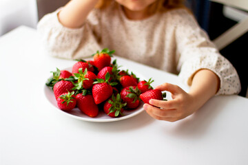 Cute little girl eating fresh strawberry in the kitchen. Healthy vitamin snack for kids. Ripe fresh berries. Harvest season. Natural vitamins .