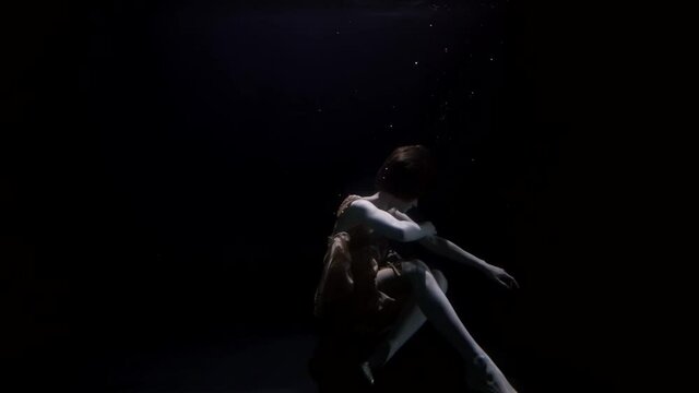 sexy lady is dressed evening dress and shoes, floating underwater inside dark and depth