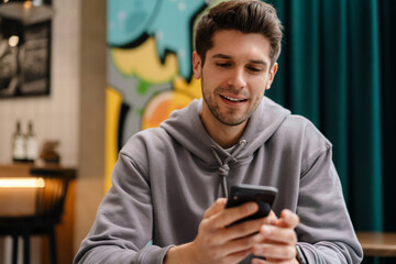 Happy young brunette man holding mobile phone
