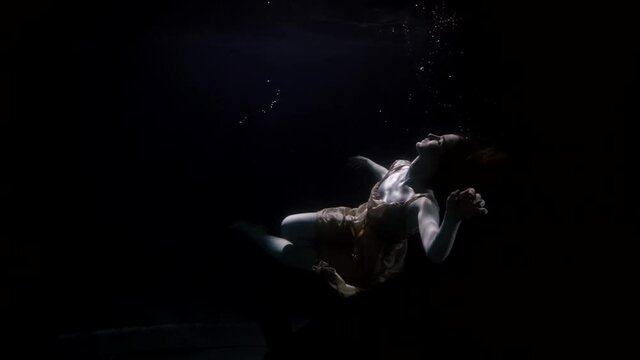 sunken woman is downing on bottom of sea or river, underwater shot of female figure in darkness and deepness