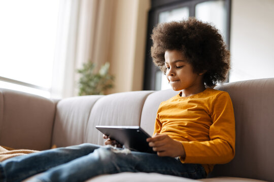 Black curly boy using tablet computer while sitting on sofa at home