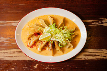 Gyoza with chicken and mushrooms in yellow curry. Pan-Asian oriental cuisine on wooden table.