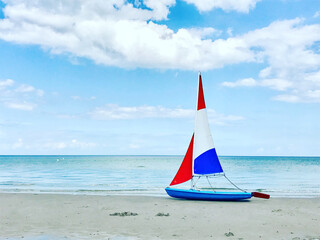 Photo of boat with colorful sails on white sand beach at cloudy weather in north Germany