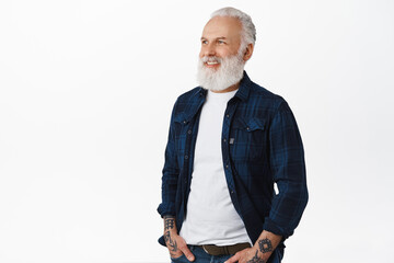 Handsome senior man with tattoos standing half-turned, looking at promotional text and smiling pleased. Old guy checking out advertisement, standing over white background