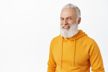 Candid happy old man with long stylish beard, laughing and smiling, looking happy, wearing modern orange hoodie, standing over white background