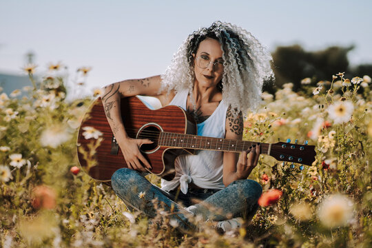 Chica delgada guapa con pelo muy rizado tocando guitarra acústica en un campo de margaritas